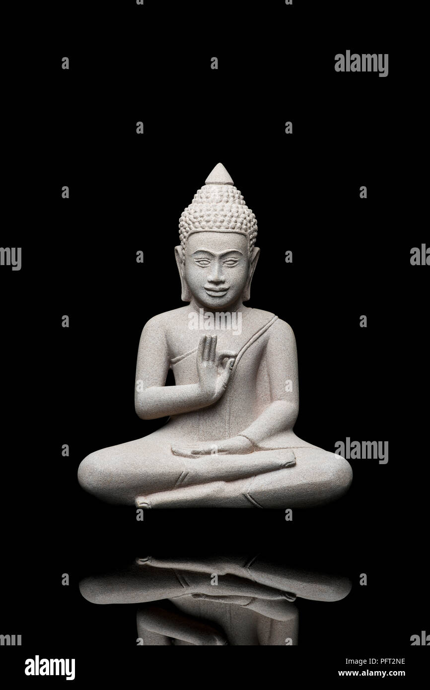 Buddha-Statuette aus hellgrauem Stein, schweben mit erhobener linker Hand, vor schwarzem Hintergrund, Erleuchtung und spiritueller Bedeutung Stockfoto