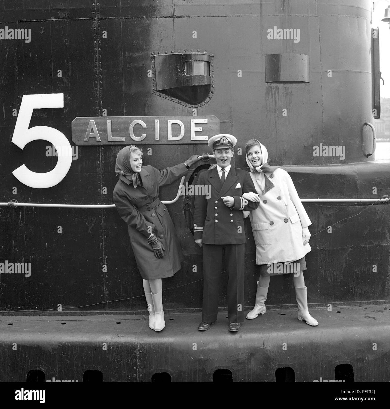 60er Jahre Mode. Zwei Models und der Kapitän der Britischen u-boot Alcide. Das U-Boot liegt im Hafen von Stockholm verankert. Die Modelle tragen die Herbste mode Mäntel und Schals. Schweden Mai 1962 Stockfoto