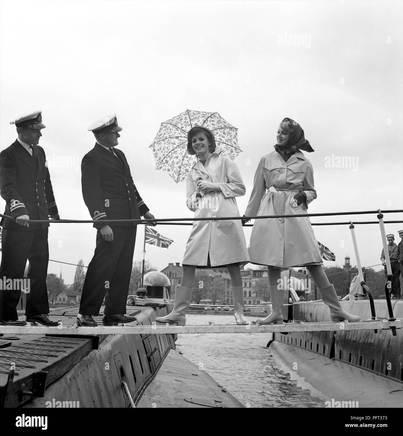 60er Jahre Mode. Zwei fashion Modelle und die Obersten der Britischen u-Boote Alcide und Orpheus. Die U-Boote im Hafen von Stockholm verankert. Die Modelle tragen die Herbste mode Mäntel und Schals. Schweden Mai 1962 Stockfoto