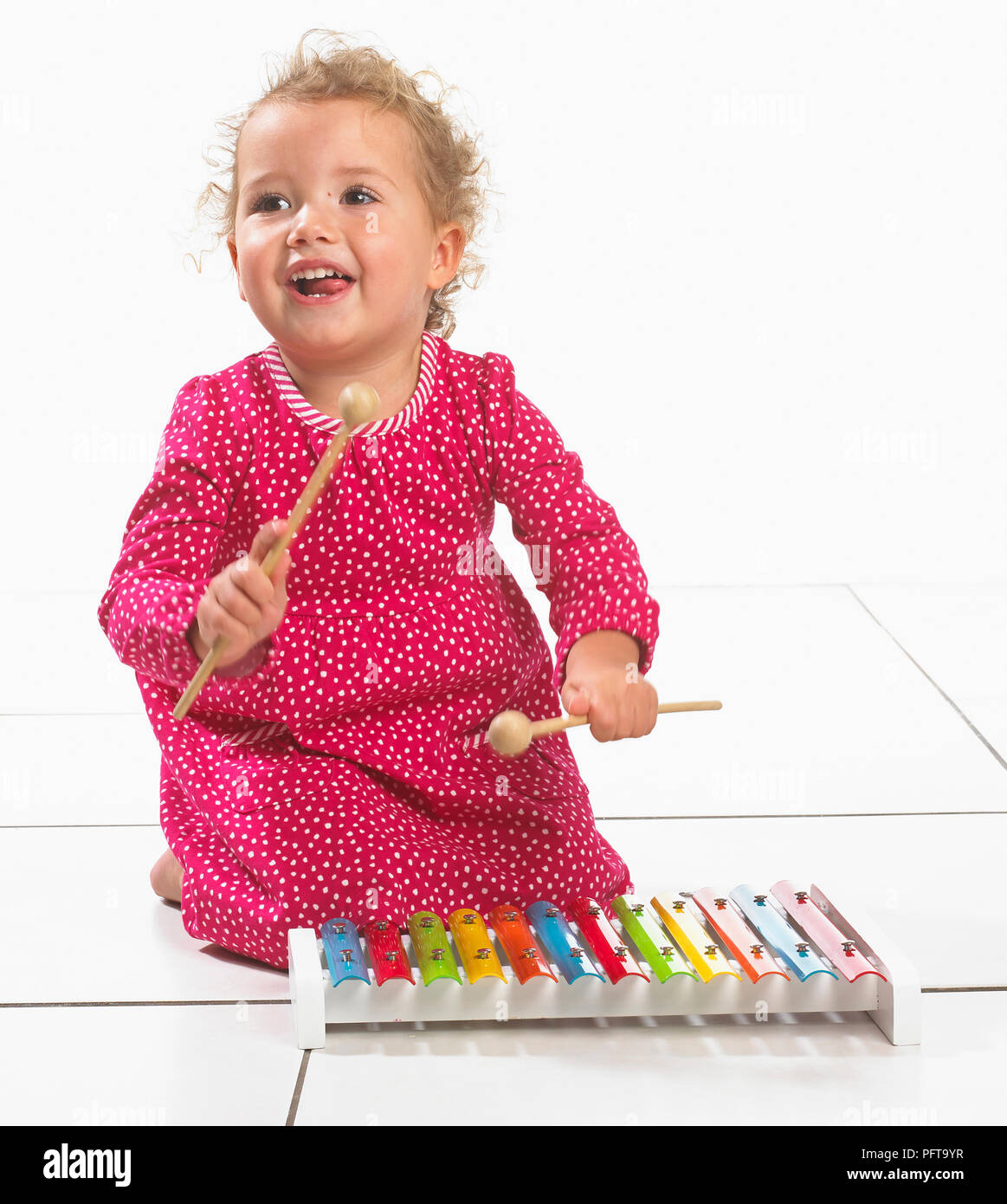 Kleines Mädchen (2 Jahre) kniend am Boden neben Xylophon Stockfoto