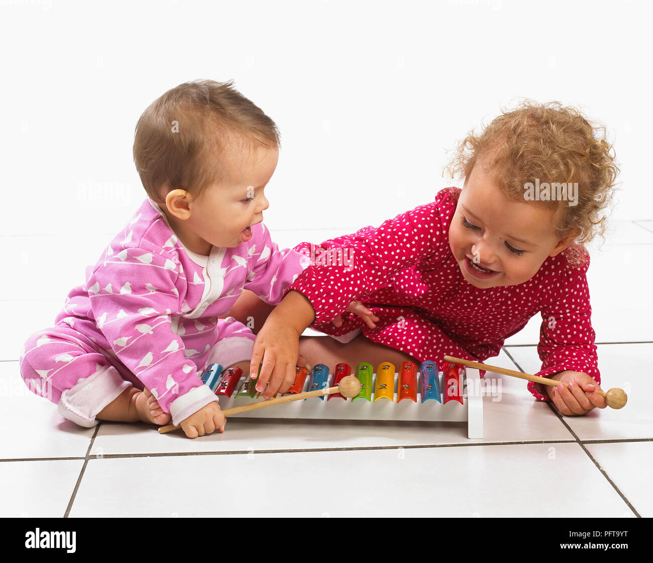 Kleines Mädchen (2 Jahre) und Baby (8 Monate) kniend auf dem Boden spielen ein Xylophon Stockfoto