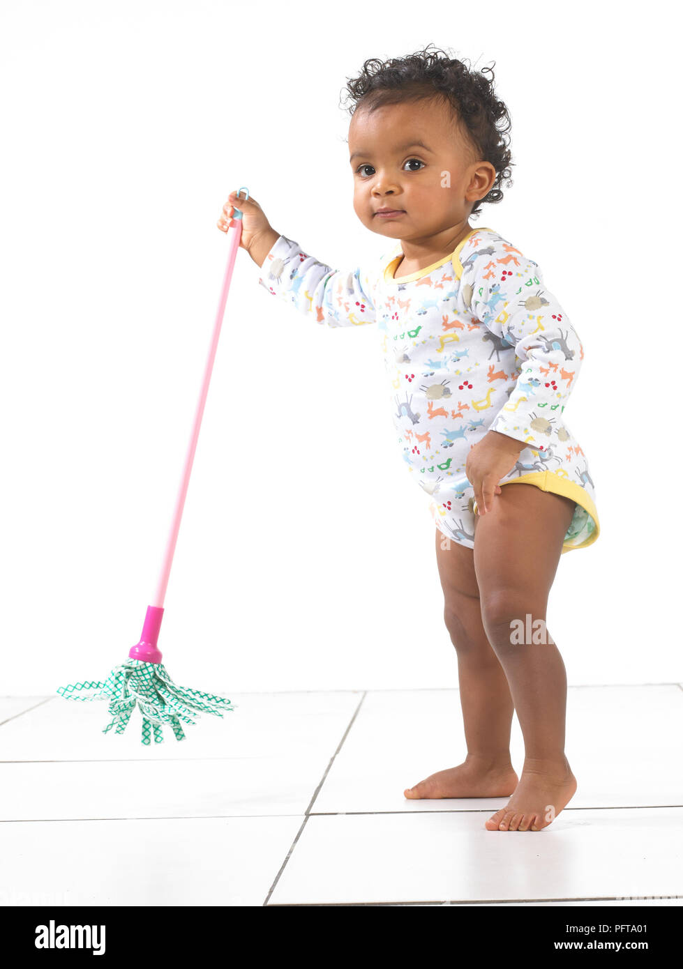 Stehendes Mädchen holding Spielzeug Mop, 18 Monate Stockfoto