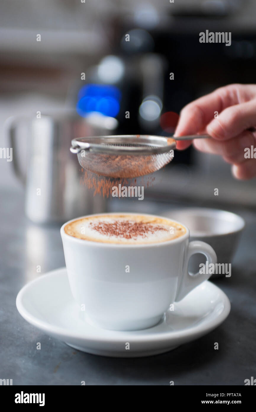 Cappuccino, mit mini Sieb zu streuen Schokolade über Kaffee Stockfoto
