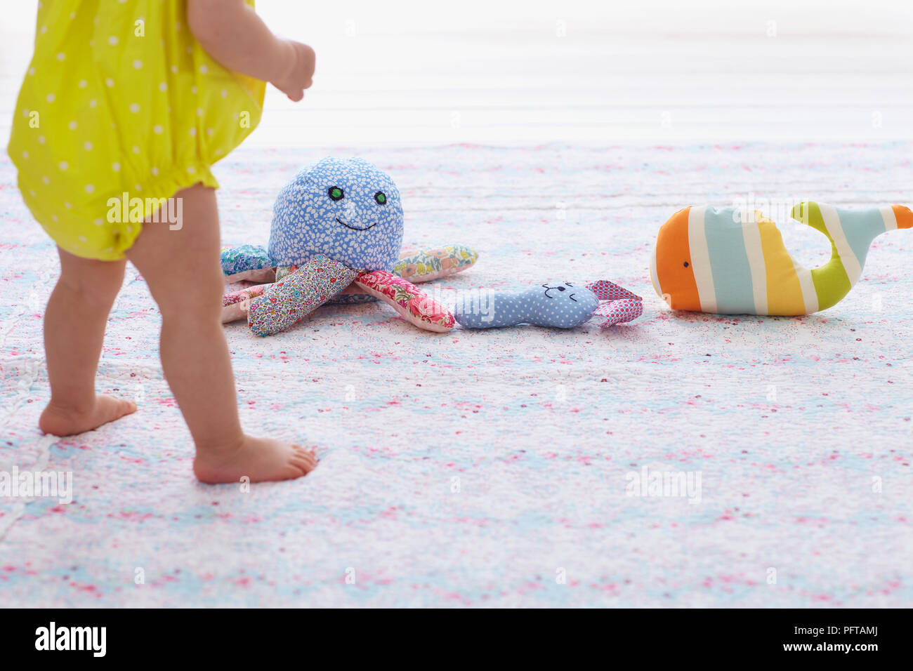 Baby Mädchen stehend suchen Bei der Auswahl der weichen Spielzeug auf dem Boden vor ihr, 13 Monate Stockfoto
