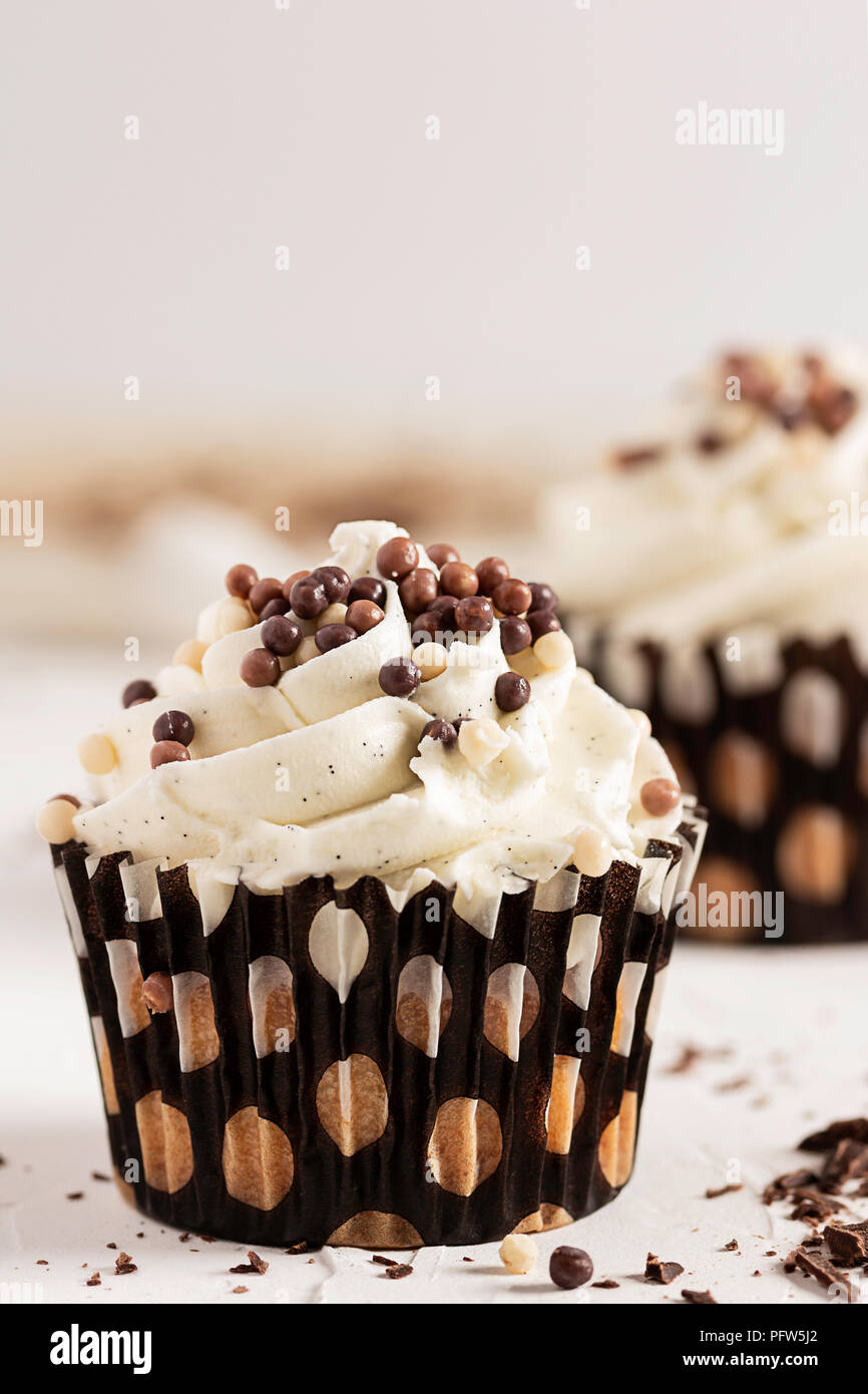Ein Vanilla Cupcake mit Schokolade Kugeln und einem anderen Cupcake in Soft Focus im Hintergrund gekleidet Stockfoto