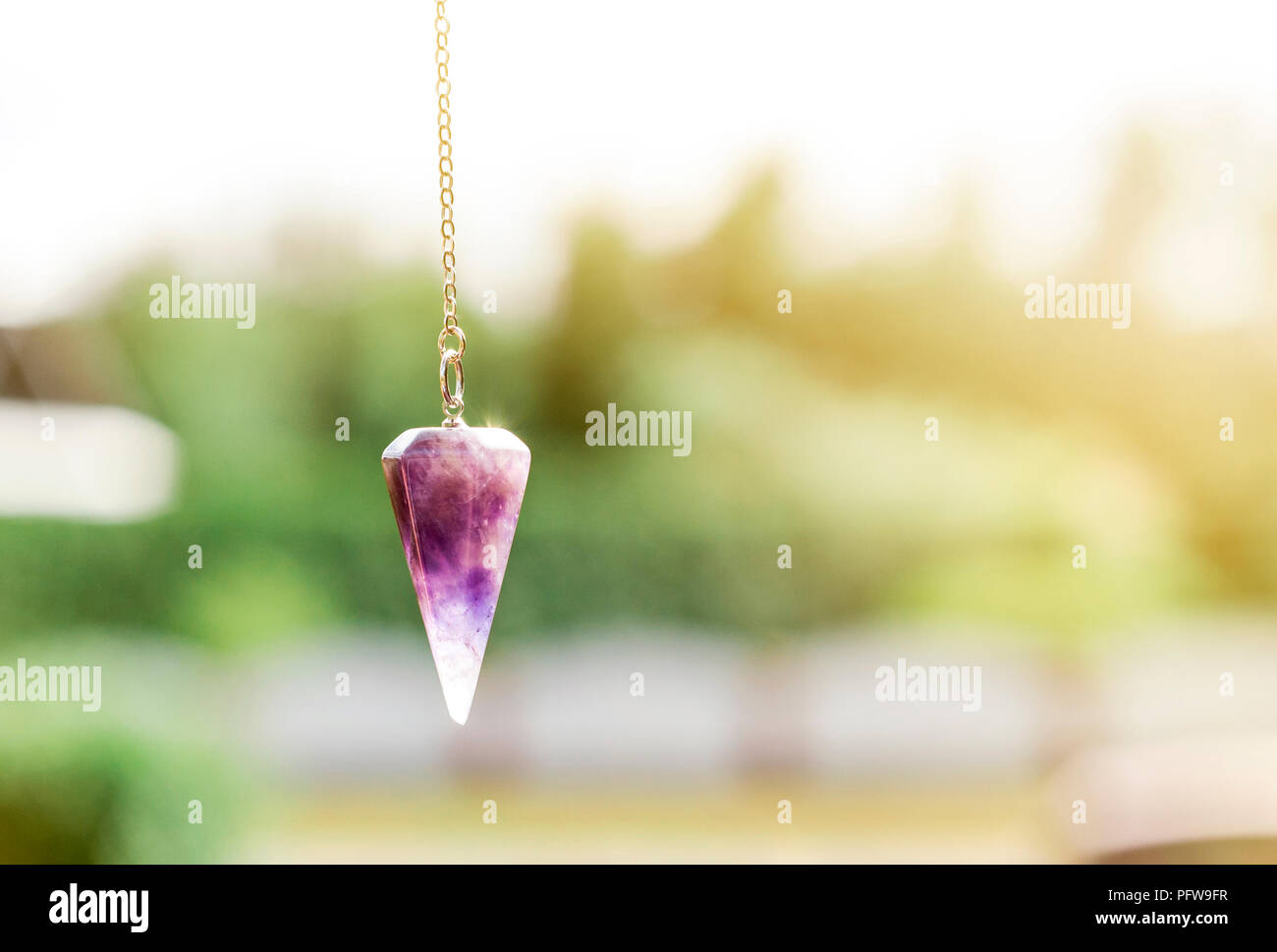Violett natürlicher Amethyst kristall Pendel, an Kette auf grüne Natur Hintergrund. Stockfoto