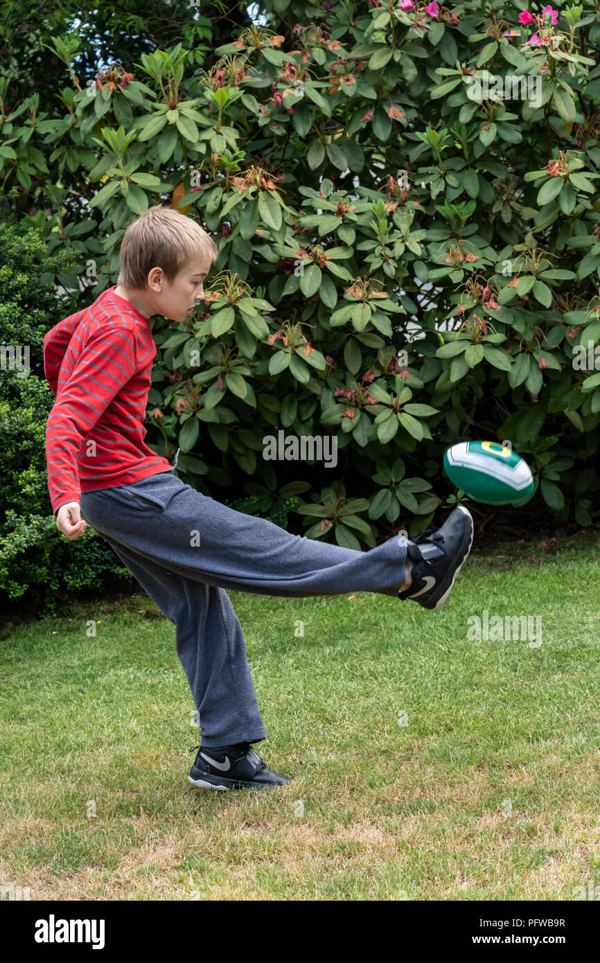 10 Jahre alter Junge Kicken eines Fußball auf seinem Rasen Stockfoto