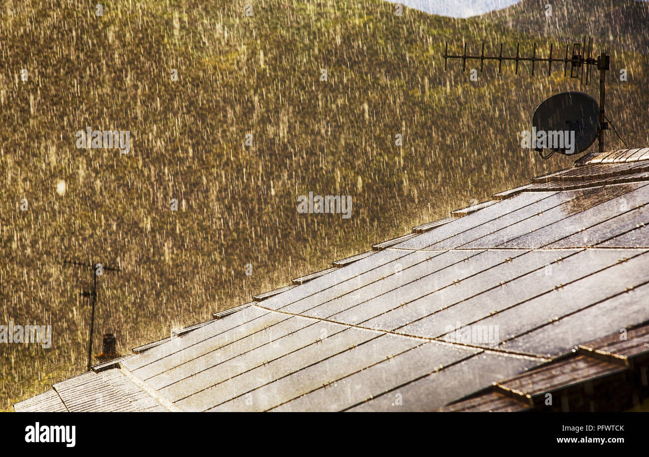 Ein Platzregen Regen Hintergrundbeleuchtung von Sonne über ein Hausdach mit eingebauten Solarzellen in Ambleside, Lake District, Großbritannien. Stockfoto