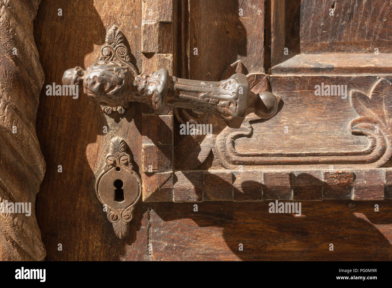 Reich verzierten alten, abgenutzten rostigem Eisen metall Türgriff und Schloss mit Schlüsselloch auf dekorative geschnitzten braunen Holztür an einem sonnigen Tag in Kotor, Montenegro. Stockfoto