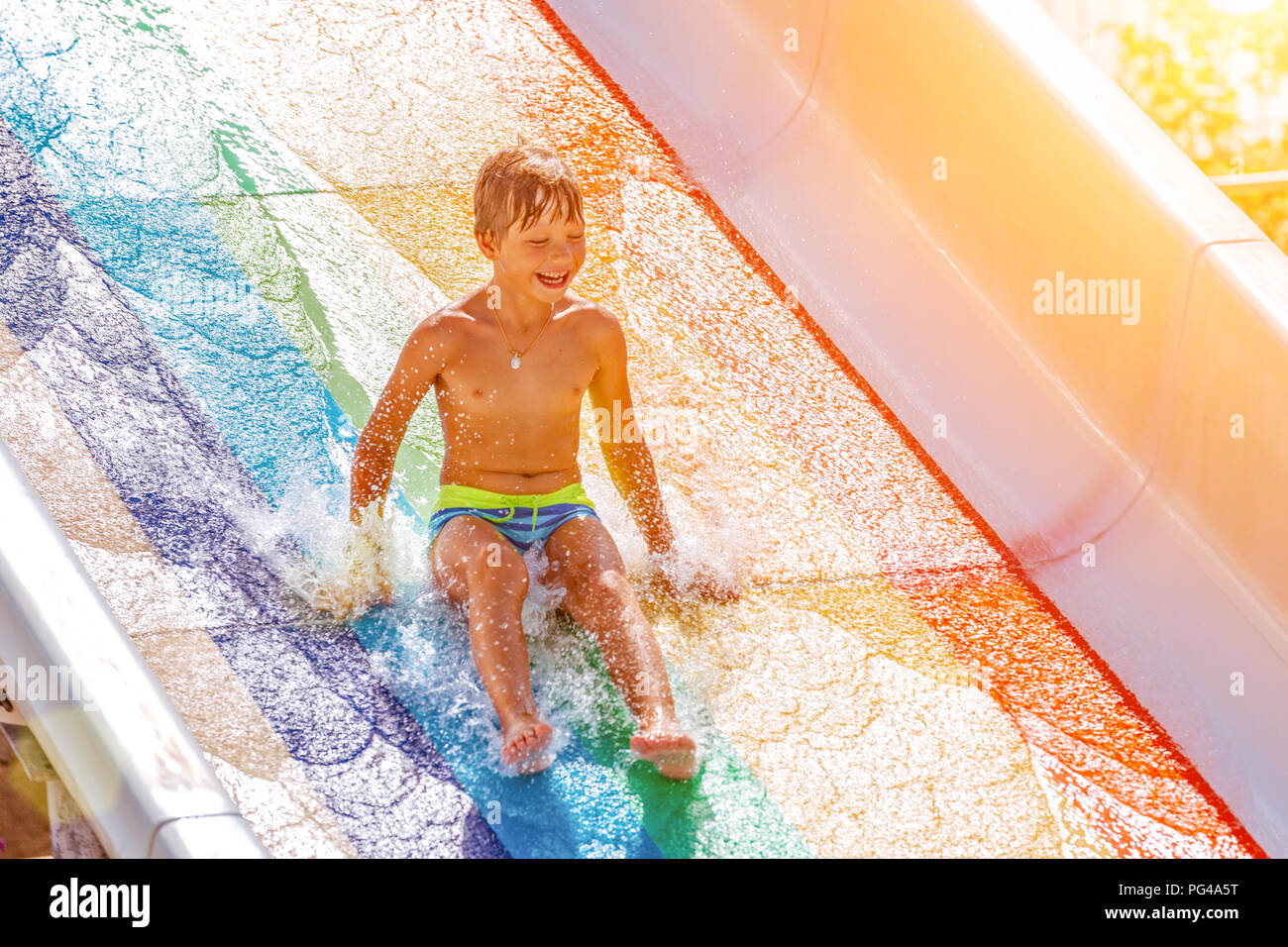 Eine glückliche junge auf Wasserrutsche in einem Schwimmbad Spaß im Sommer Urlaub in einer schönen Aqua Park. Ein Junge nach unten kriechend auf der Wasserrutsche und spritzt. Stockfoto