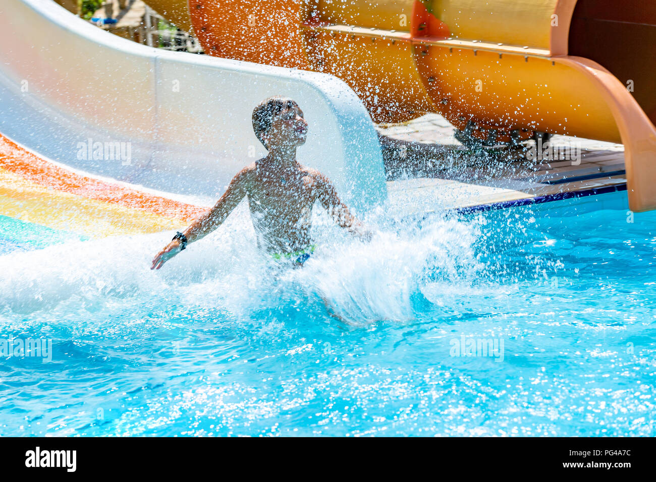 Eine glückliche junge auf Wasserrutsche in einem Schwimmbad Spaß im Sommer Urlaub in einer schönen Aqua Park. Ein Junge nach unten kriechend auf der Wasserrutsche und spritzt. Stockfoto