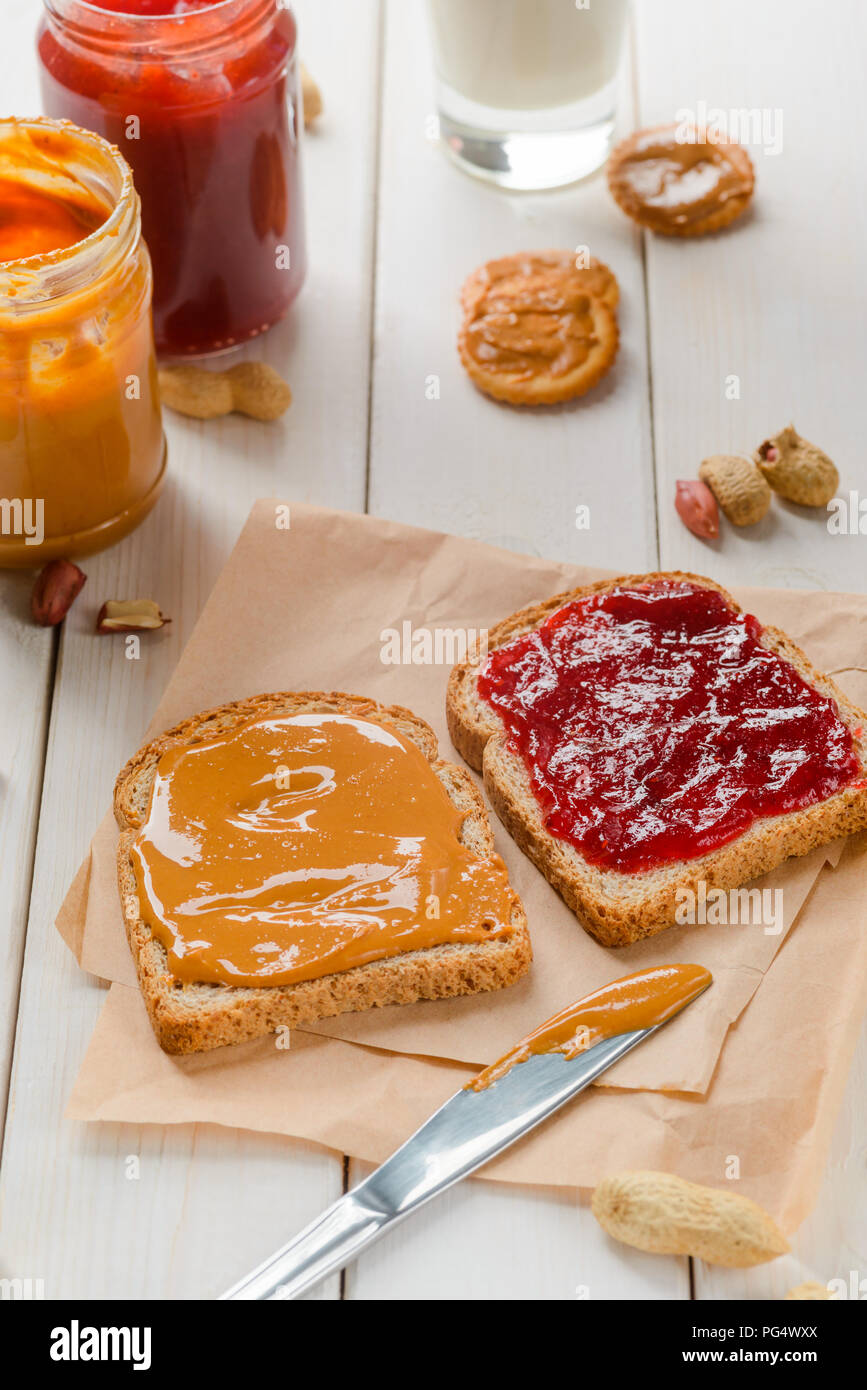 Traditionelle Sandwich auf Backpapier, close-up. Peanut Butter und Marmelade Gläser, Cracker und Glas pf Milch auf dem Hintergrund. Stockfoto