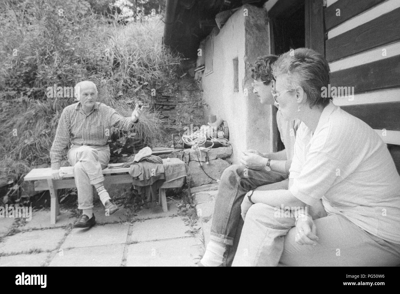 Der Schriftsteller Bohumil Hrabal auf einer Bank vor dem Haus des Malers Josef Jira. Rechts im Vordergrund ist der Übersetzer Susanna Roth. Stockfoto