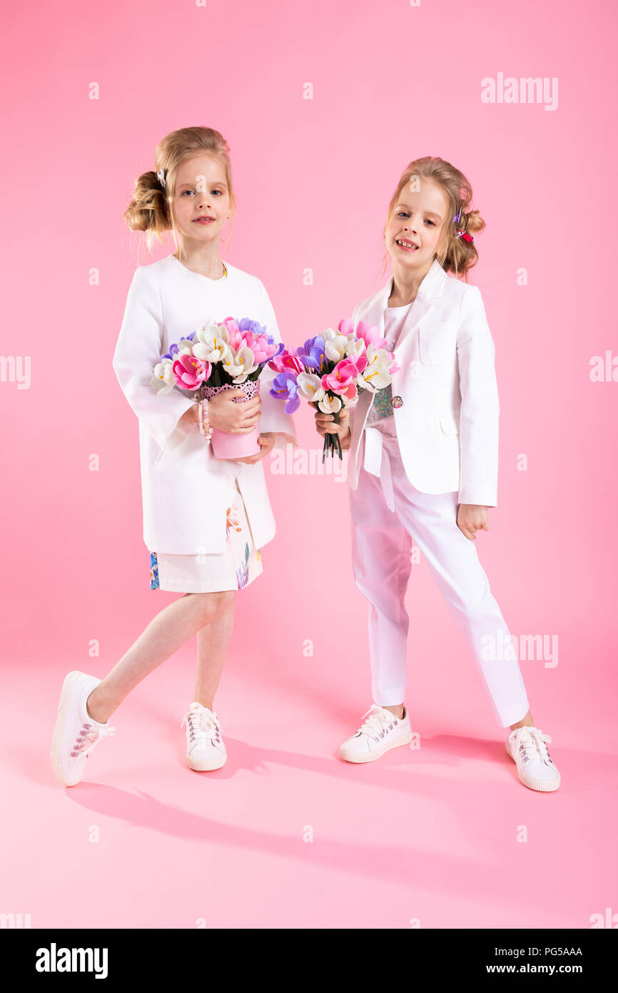 Zwillinge Mädchen in leichter Kleidung mit blumensträussen stehen auf einem  rosa Hintergrund Stockfotografie - Alamy