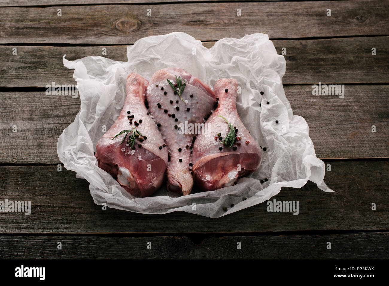 Raw Türkei Beine mit Pfefferkörner und Rosmarin auf Backpapier auf hölzernen Tischplatte Stockfoto