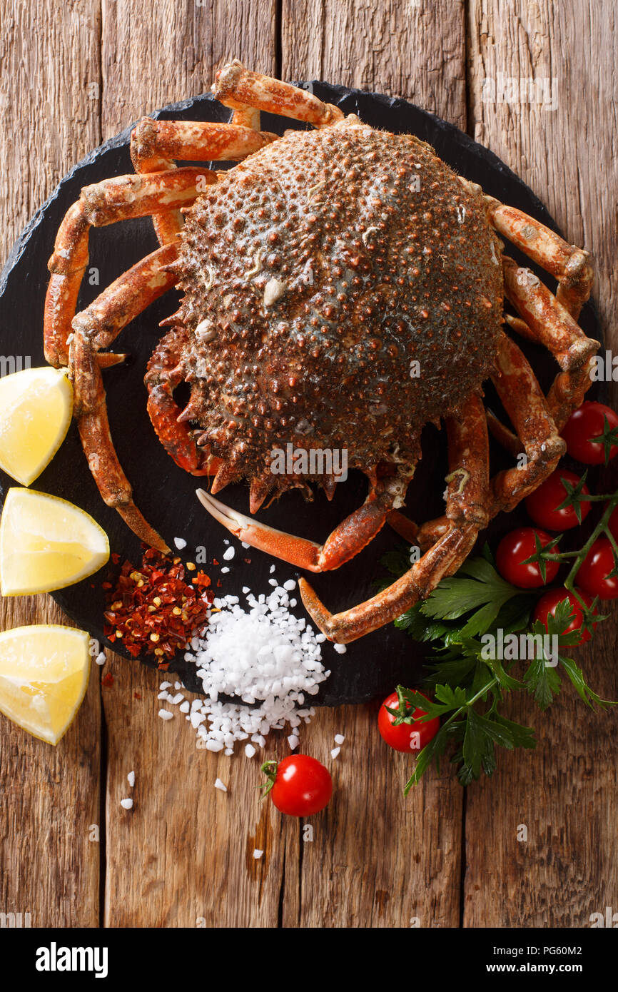 Luxuriöse Raw Seespinne durch frische Tomaten, Zitrone, Kräuter und Gewürze in der Nähe umgeben auf einem schwarzen Stein. Vertikal oben Ansicht von oben Stockfoto