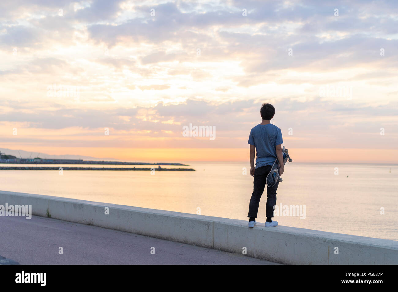 Junge chinesische Mann mit Skateboard stehend an der Wand am Strand Stockfoto