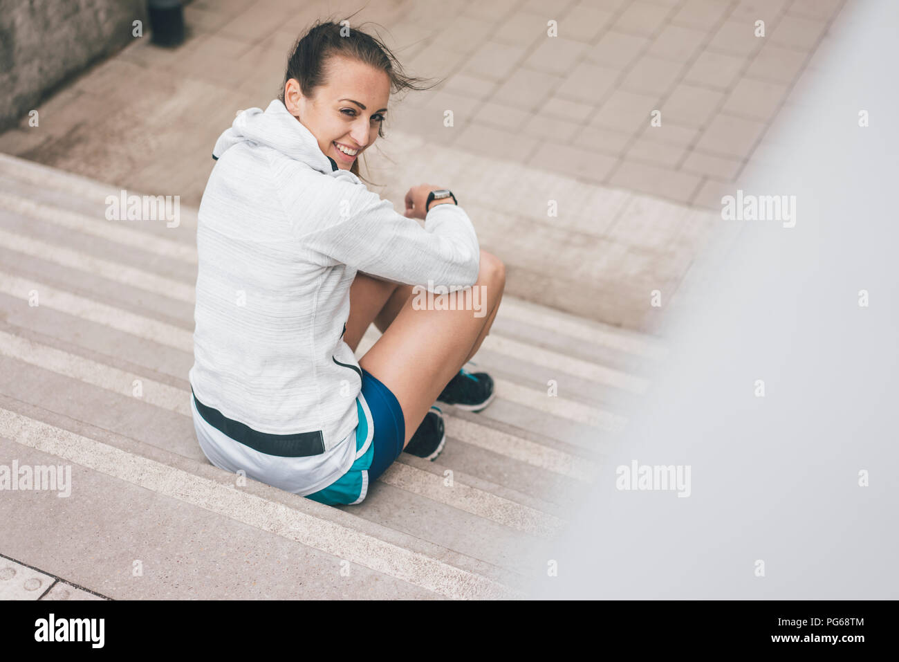 Lächelnd sportliche junge Frau sitzt auf der Treppe im Freien Stockfoto