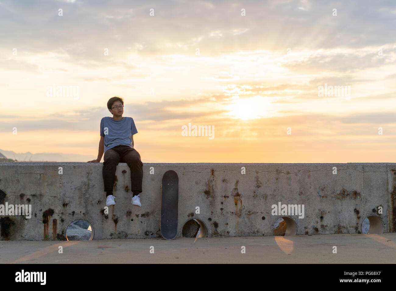 Junge chinesische Mann sitzt auf der Wand bei Sonnenaufgang Stockfoto