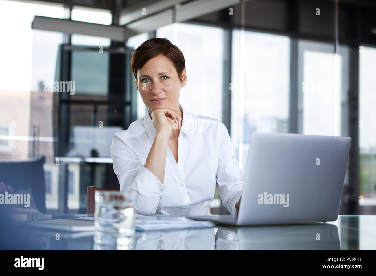 Portrait von zuversichtlich Geschäftsfrau am Glastisch im Büro mit Laptops Stockfoto