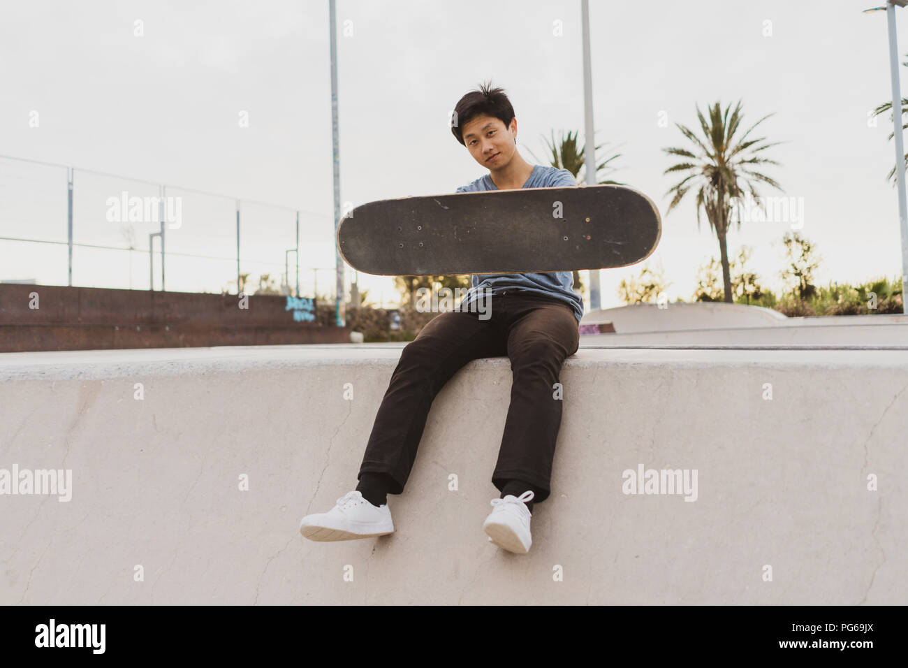 Junge chinesische Mann sitzt auf die Wand von einem Skate Park in der Nähe des Strandes Stockfoto