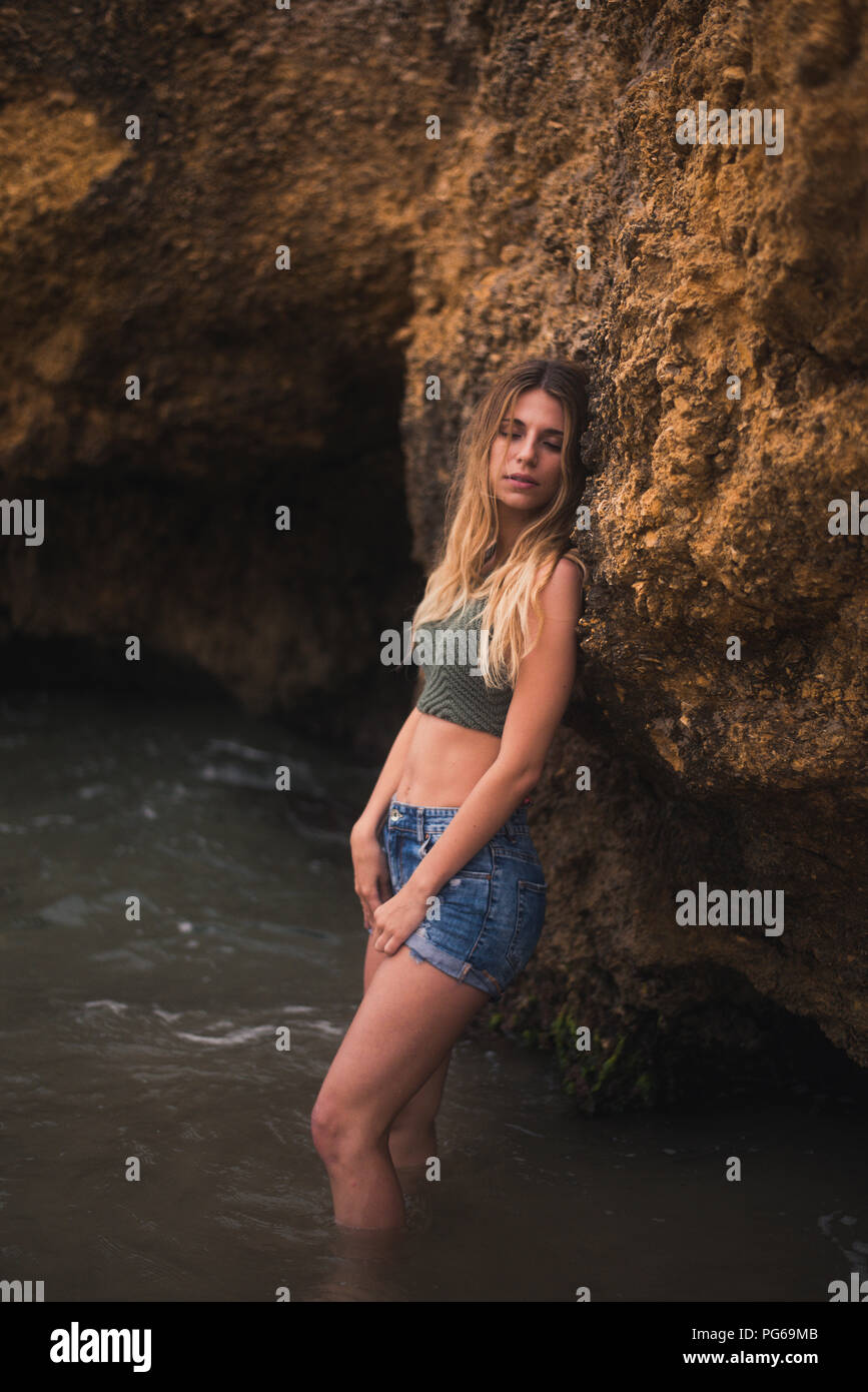 Schöne junge Frau, die auf einem Felsen im Meer Stockfoto