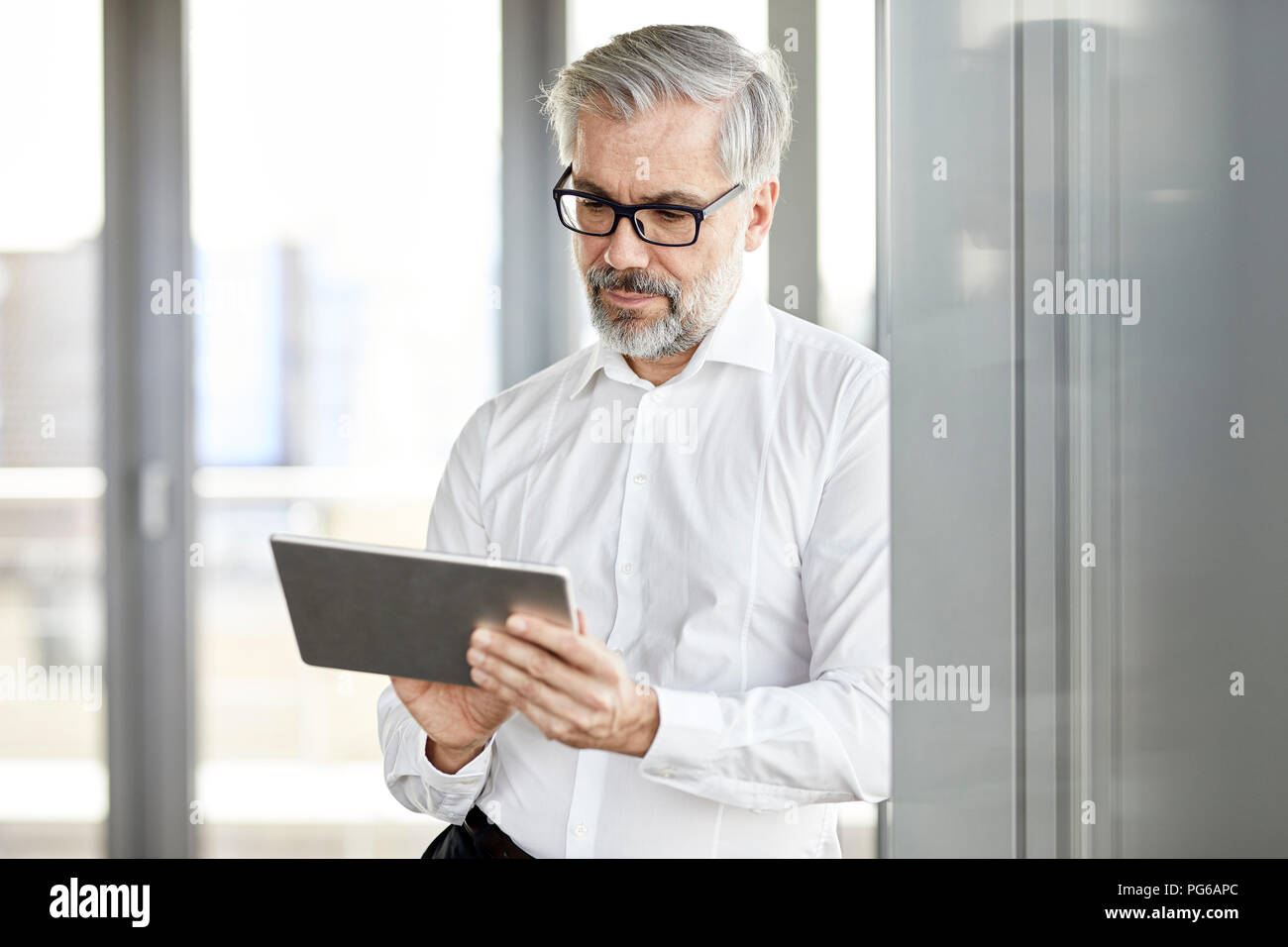 Unternehmer stehen am Fenster mit Tablet Stockfoto