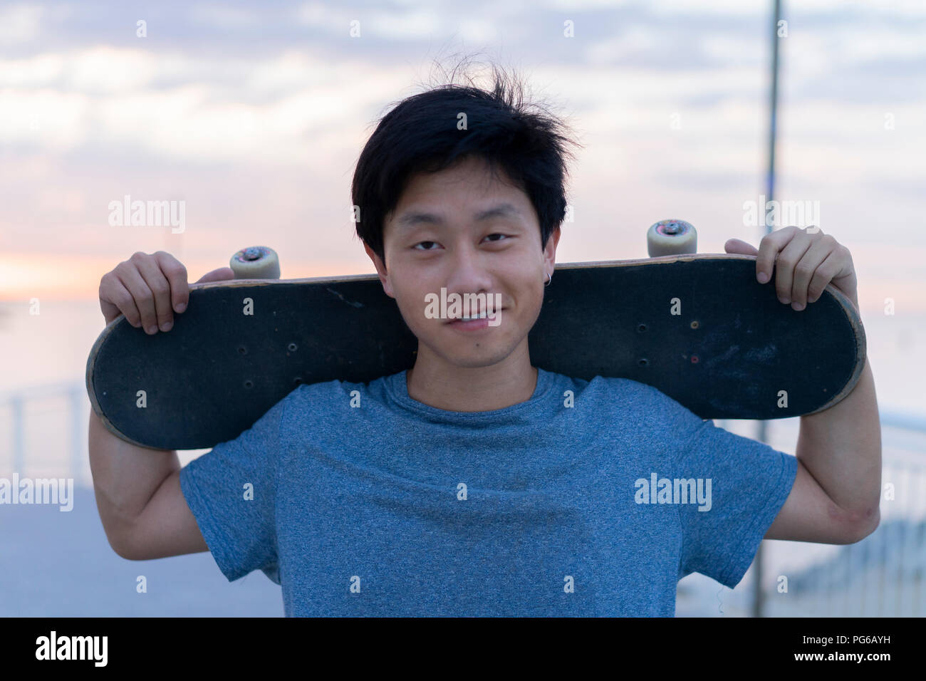 Junge chinesische Mann mit Skateboard am Strand bei Sonnenaufgang Stockfoto