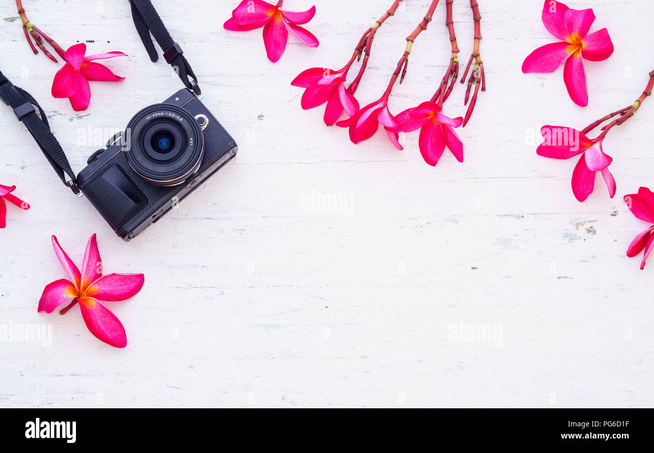 Schwarz Kamera mit rosa Flora Blumen auf dem Grunge weiß Holz- Hintergrund. Flach der Reise Zubehör Hintergrund Konzept. Stockfoto