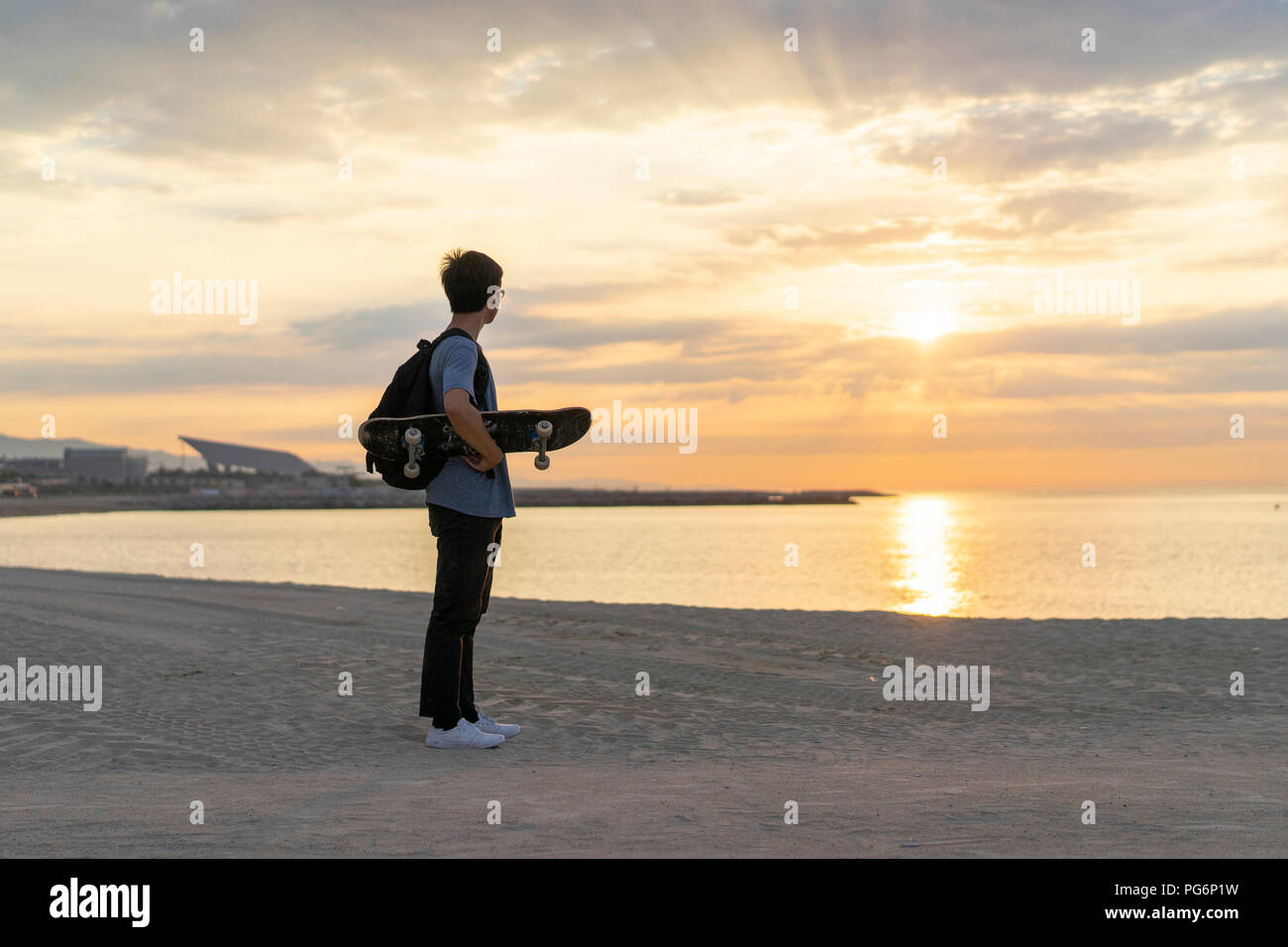 Junge chinesische Mann mit Skateboard stehen am Strand bei Sonnenaufgang Stockfoto