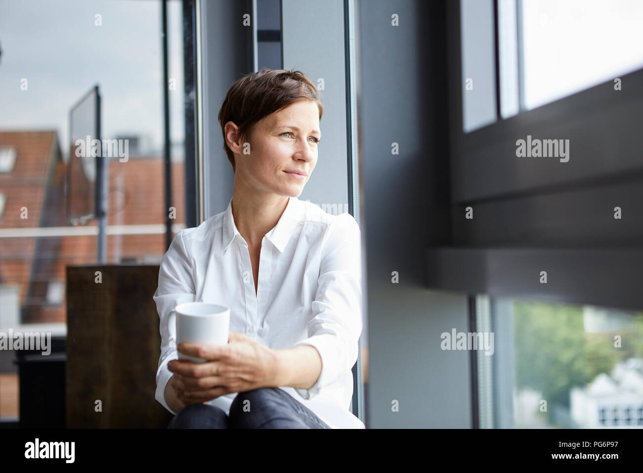 Geschäftsfrau im Büro mit Tasse Kaffee Blick aus Fenster Stockfoto