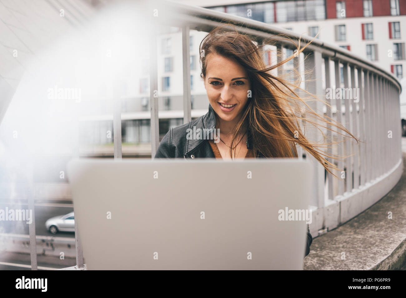 Portrait von lächelnden jungen Frau mit windswept mit Laptop auf der Autobahn Brücke Haar Stockfoto