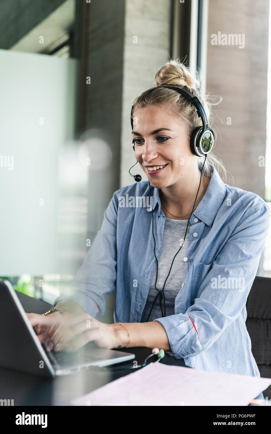 Junge geschäftsfrau am Schreibtisch sitzend, einen Anruf zu tätigen, die mit dem Headset und Laptop Stockfoto