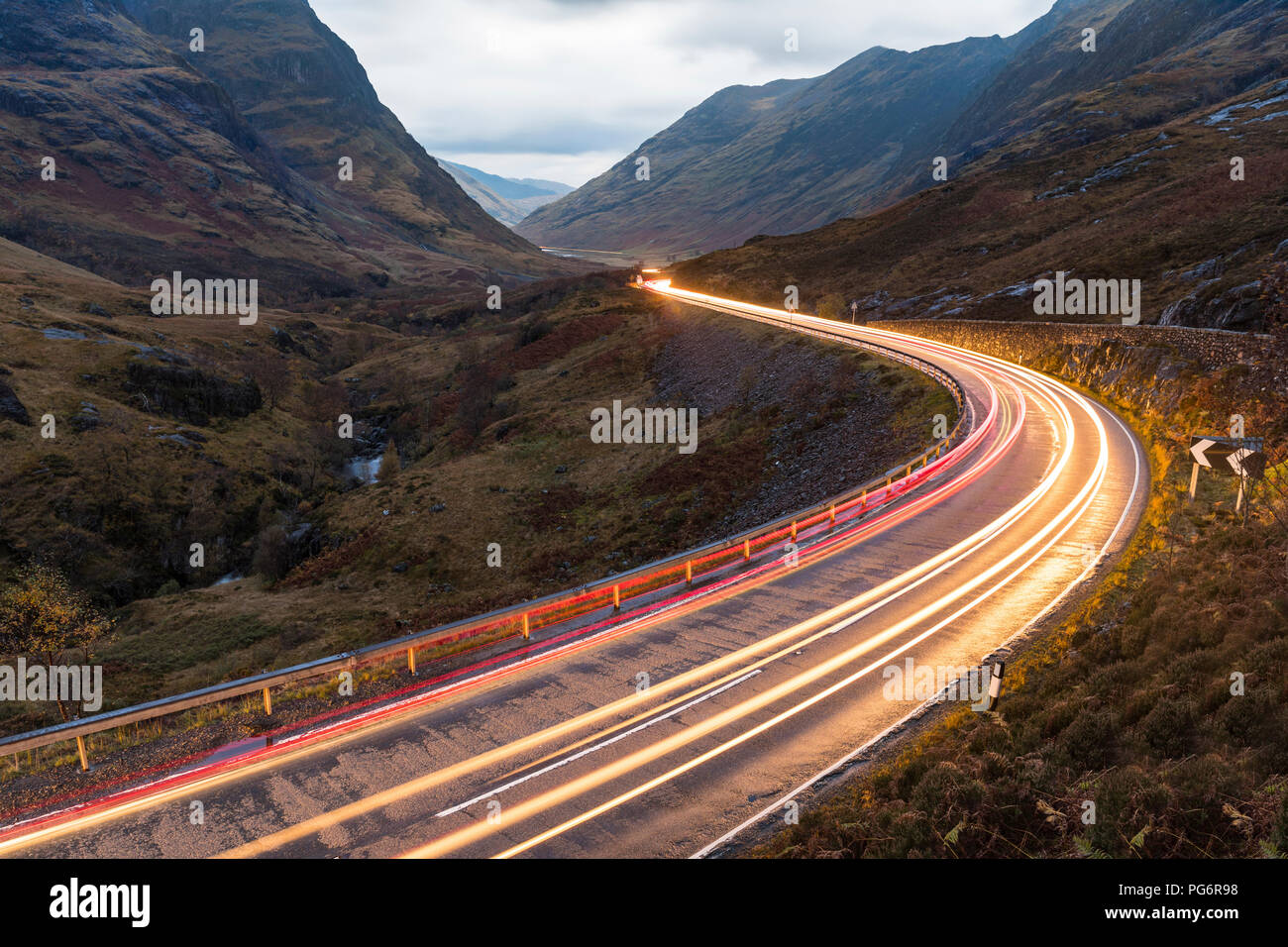 Großbritannien, Schottland, Auto Licht Wanderwege auf malerische Straße durch die Berge in den schottischen Highlands in der Nähe von Glencoe in der Dämmerung Stockfoto