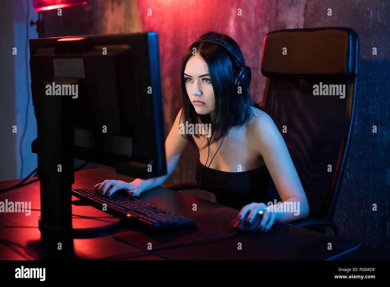 Schöne junge Mädchen mit Brille und Gaming Headset spielt online Spiel auf Gaming-PC im dunklen Bereich. Streaming online Spiele auf Internet Stockfoto