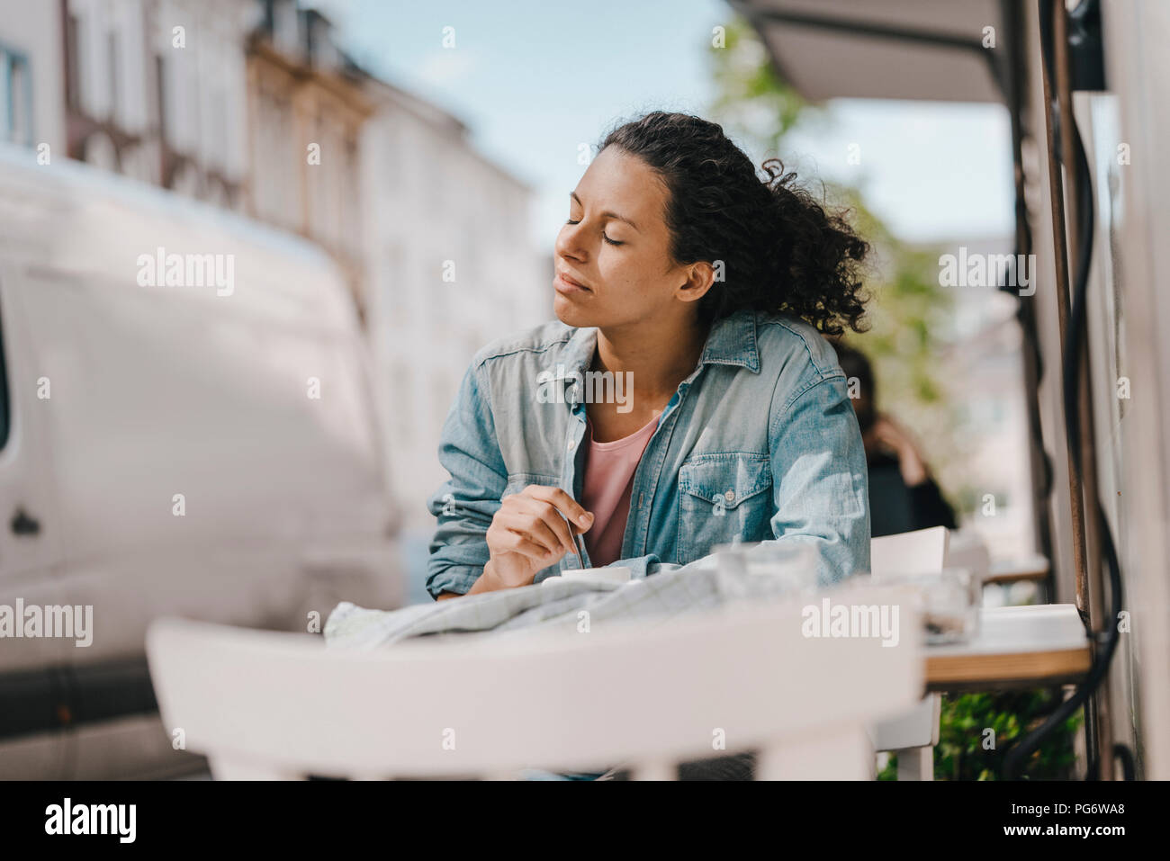 Junge Frau vor Café sitzen mit geschlossenen Augen, die Sonne genießen Stockfoto