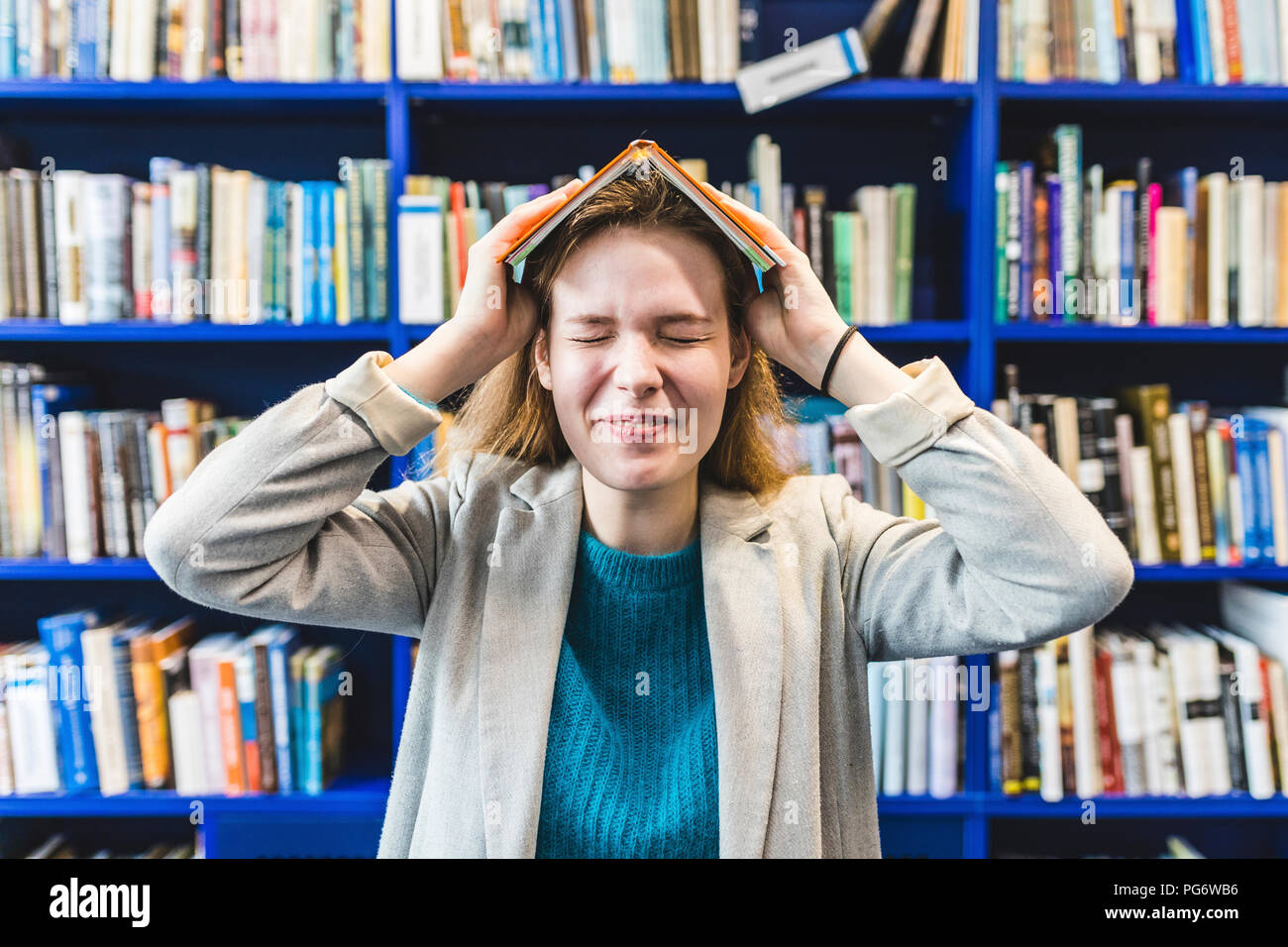 Portrait von jugendlichen Mädchen mit Buch auf dem Kopf in einer öffentlichen Bibliothek Stockfoto