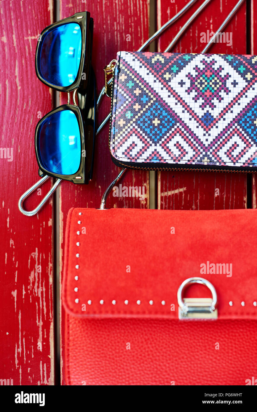 Sonnenbrille, Geldbeutel und Handtaschen auf der roten Bank aus Holz Stockfoto