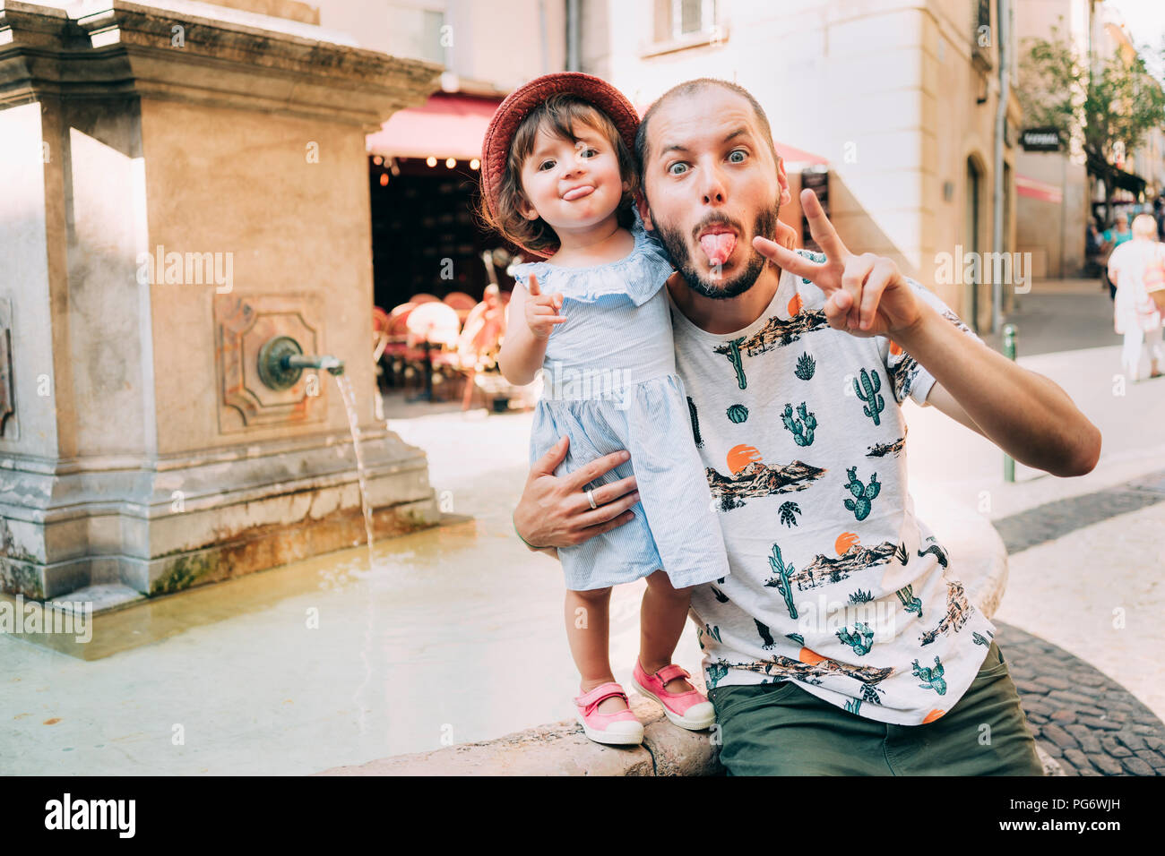 Frankreich, Aix-en-Provence, lustige Kleinkind Mädchen und Vater mit herausgestreckter Zunge neben einem Springbrunnen in der Stadt Stockfoto
