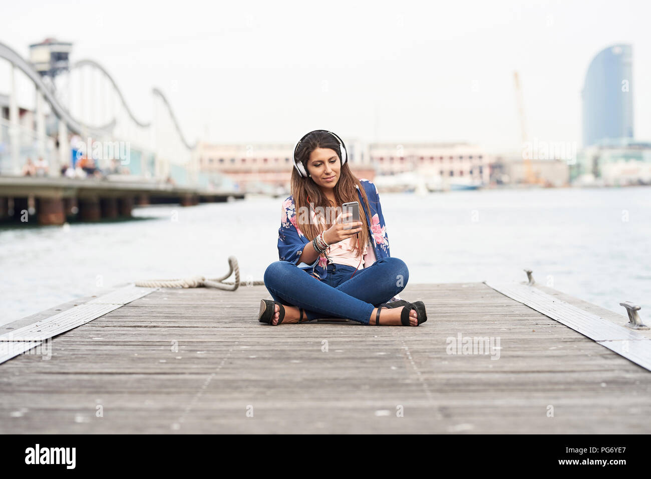 Spanien, Barcelona, Portrait von Inhalt Frau mit Kopfhörer sitzen auf Mole in Zelle Telefon Stockfoto