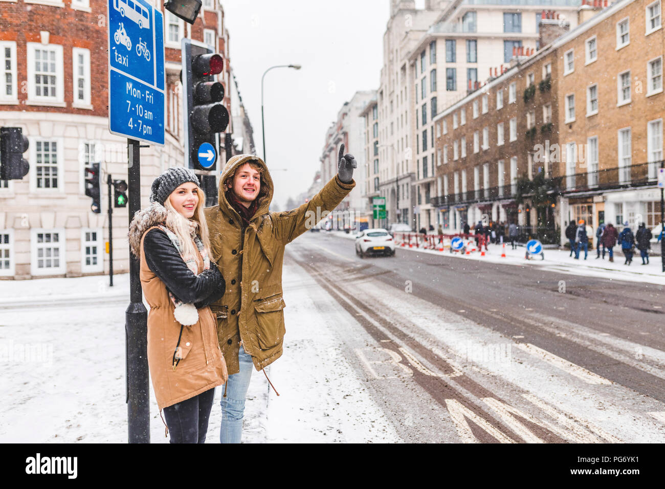 UK, London, junges Paar am Straßenrand hageln Taxi im Winter Stockfoto