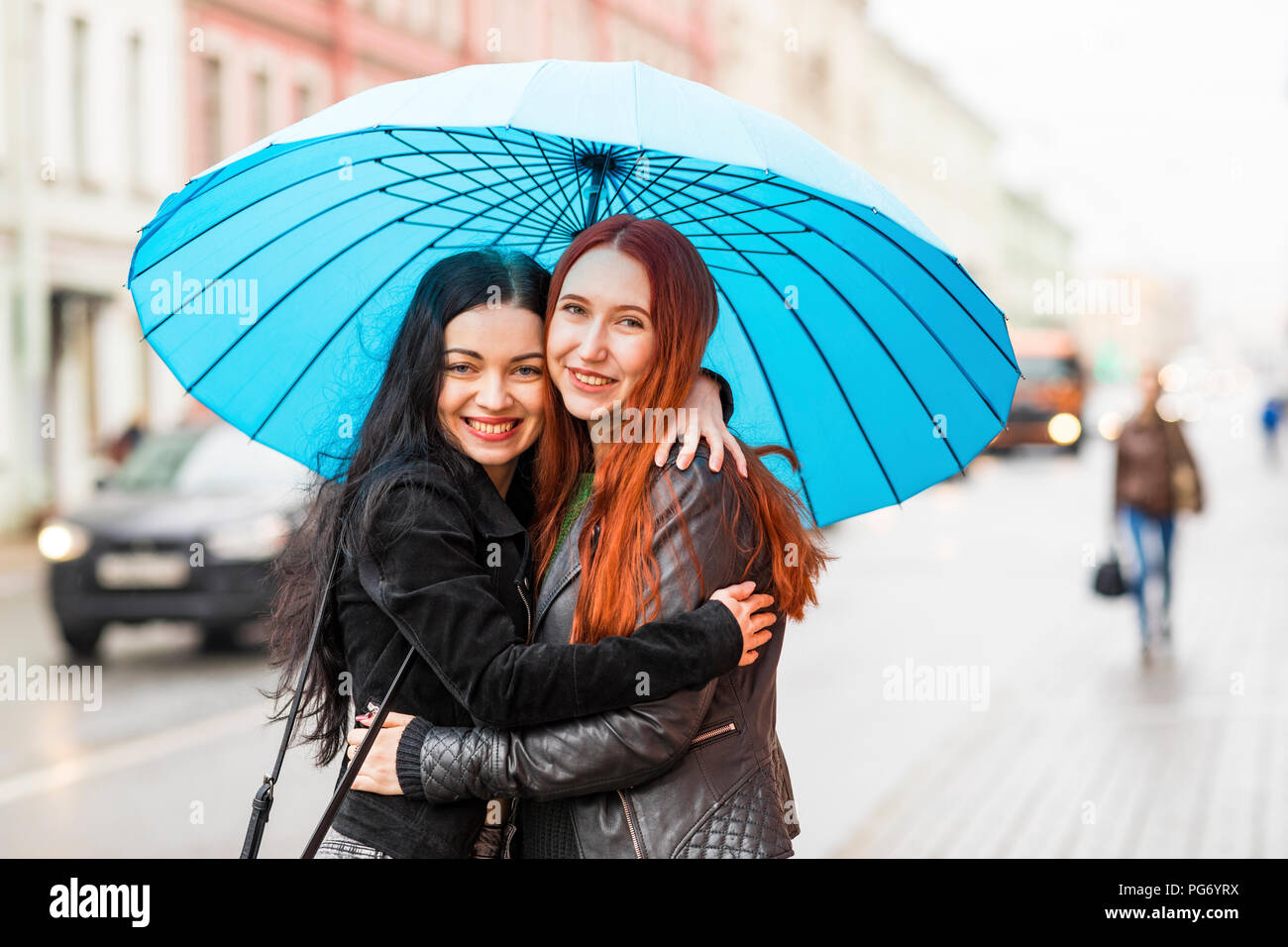 Zwei glückliche Frauen umarmen in der Stadt an einem regnerischen Tag Stockfoto
