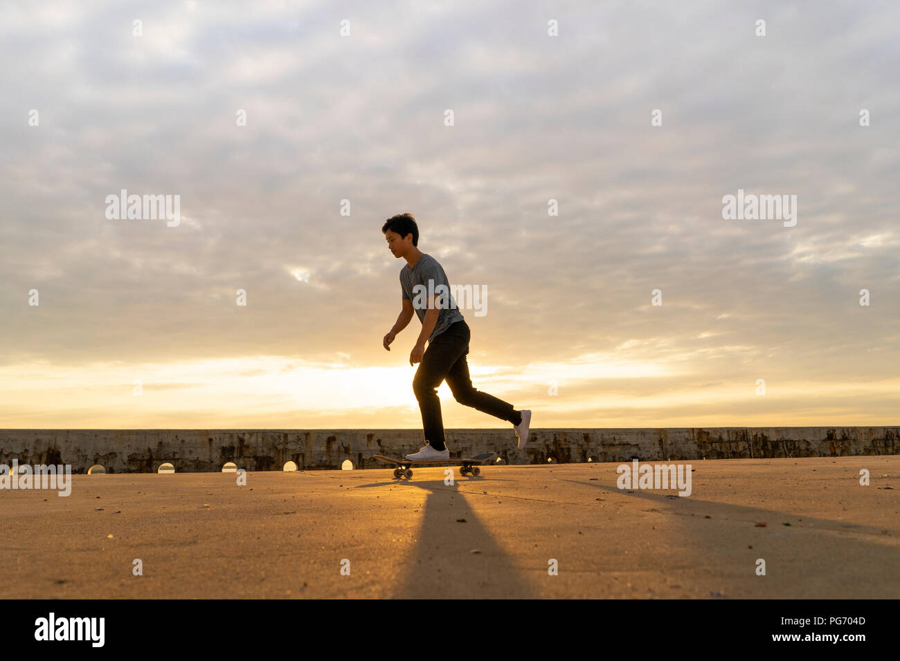 Junge Chinesen skateboarding an sunsrise nahe dem Strand Stockfoto
