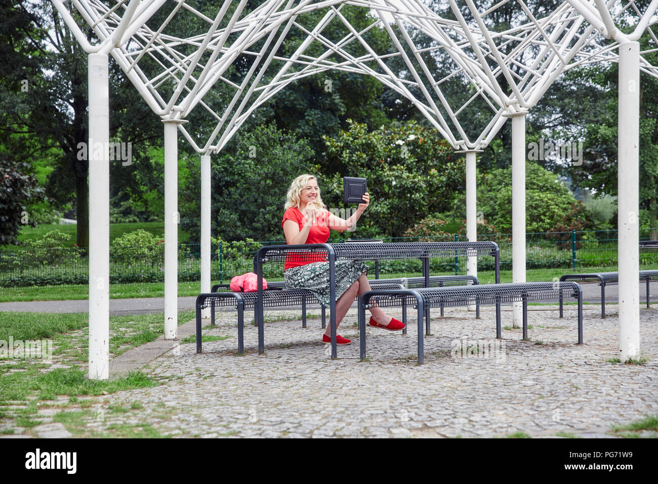 Lächelnd schwangere Frau auf einer Parkbank ein selfie mit einem Tablet Stockfoto