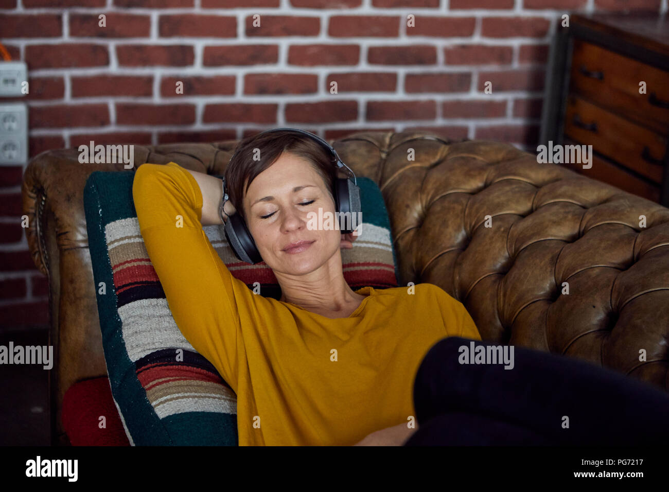 Frau mit Kopfhörer auf dem Sofa liegend, Musik hören Stockfoto