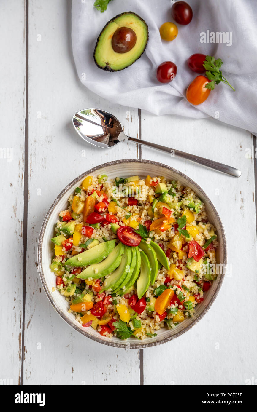 Schüssel mit Bulgur Salat mit Paprika, Tomaten, Avocado, Frühlingszwiebeln und Petersilie Stockfoto