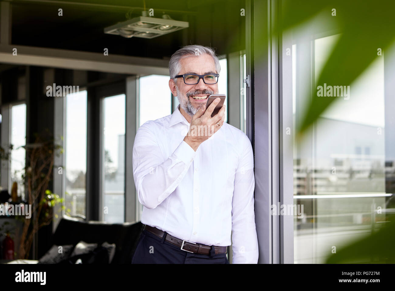 Lächelnd Geschäftsmann an französische Tür mit Handy Stockfoto