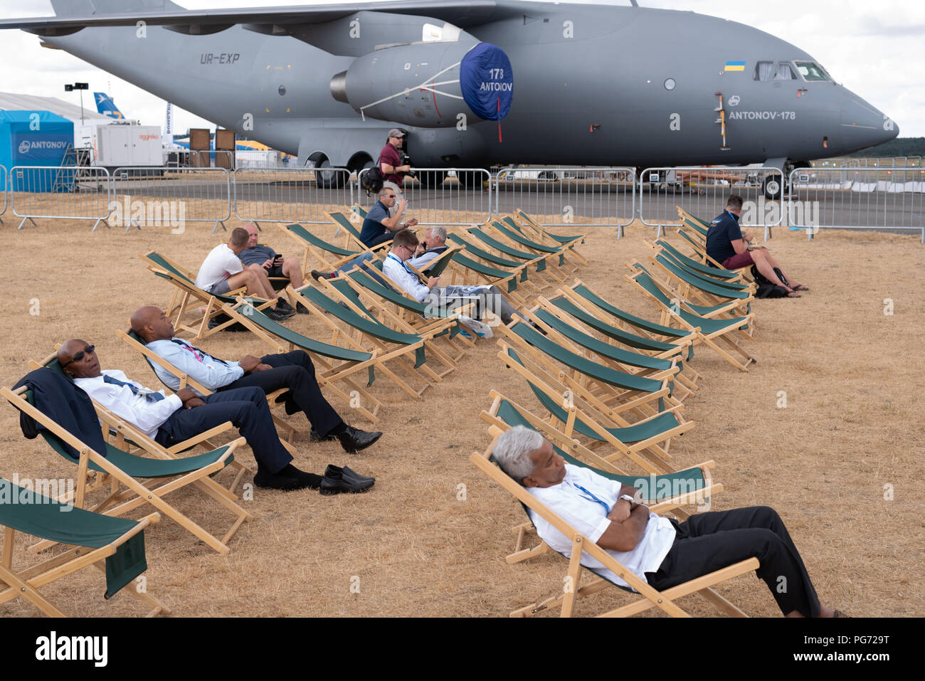 Entspannen Sie in Liegestühlen auf der Farnborough Airshow mit einer russischen Antonov 178 in Hintergrund und verbrannte Gras von der Sommerhitze Stockfoto