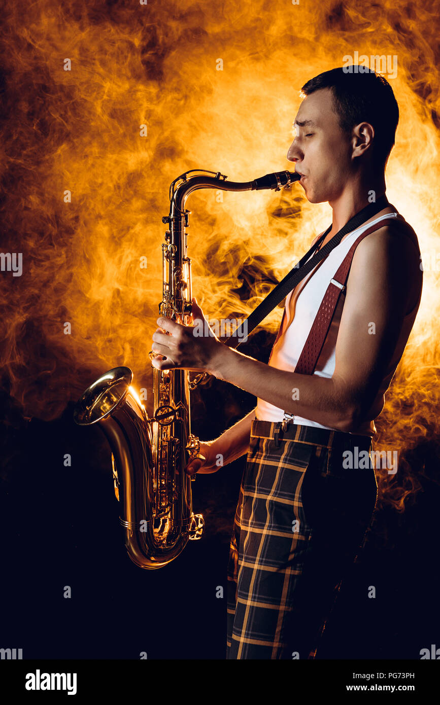 Seitenansicht der expressiven stilvolle junge Musiker Saxophon spielen in Rauch Stockfoto