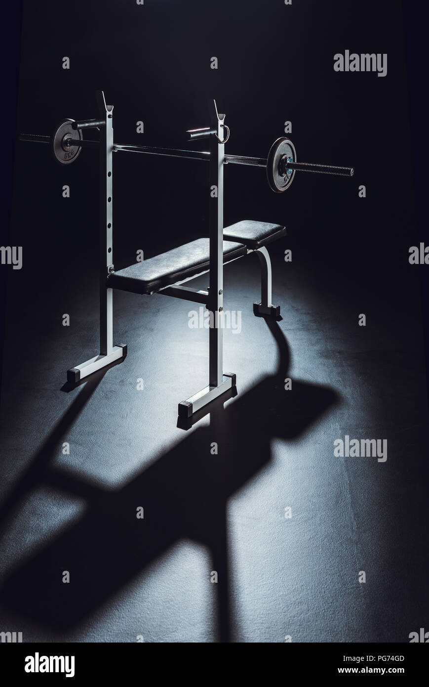 Langhantelstange mit Schatten auf dem Boden im Fitnessstudio, schwarzer Hintergrund Stockfoto
